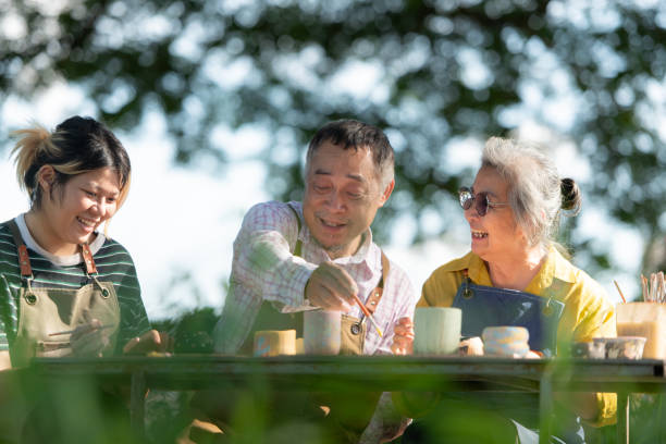 An elderly couple and instructor painting ceramics outside
